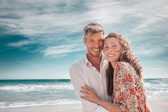 Vorsorge - Paar mittleren Alters am Strand lächelt in die Kamera